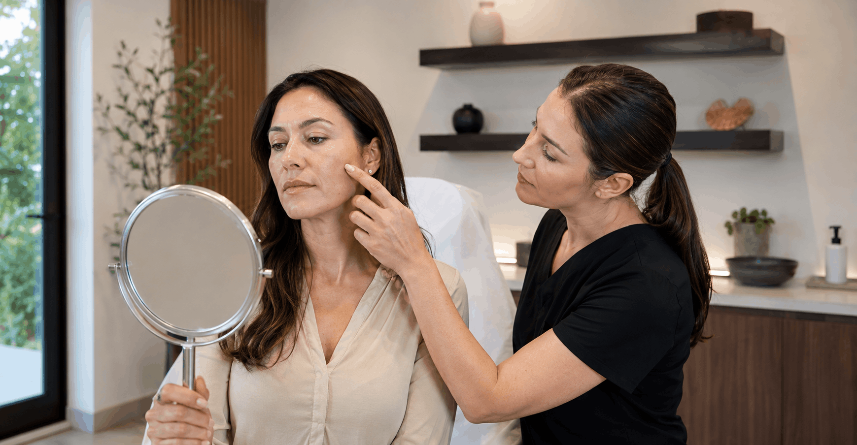 aesthetic provider discussing facial skin concerns with a patient using a handheld mirror during a consultation.