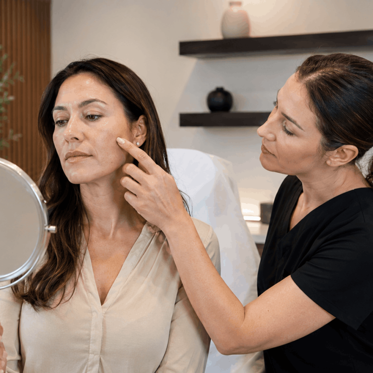 Aesthetic provider discussing facial skin concerns with a patient using a handheld mirror during a consultation.